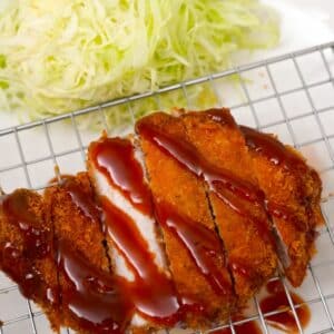 Pork Katsu covered with katsu sauce on a plate next to a bed of shredded cabbage.