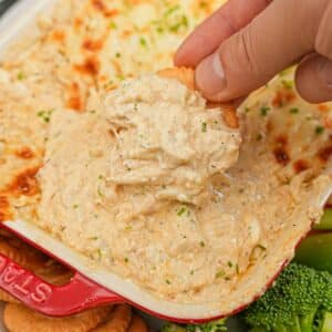 Hot Baked Crab Dip with mozarella cheese in a baking dish being scooped by a cracker.