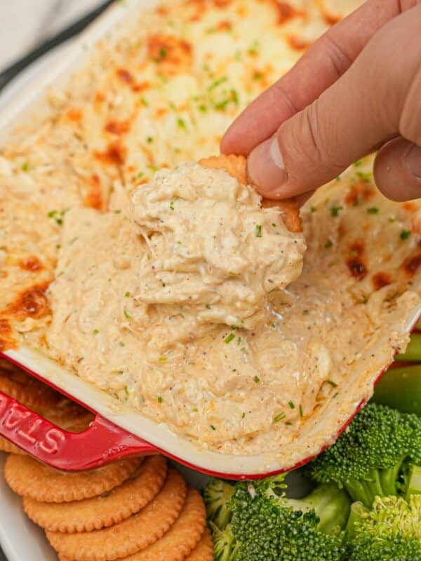 Hot Baked Crab Dip with mozarella cheese in a baking dish being scooped by a cracker.