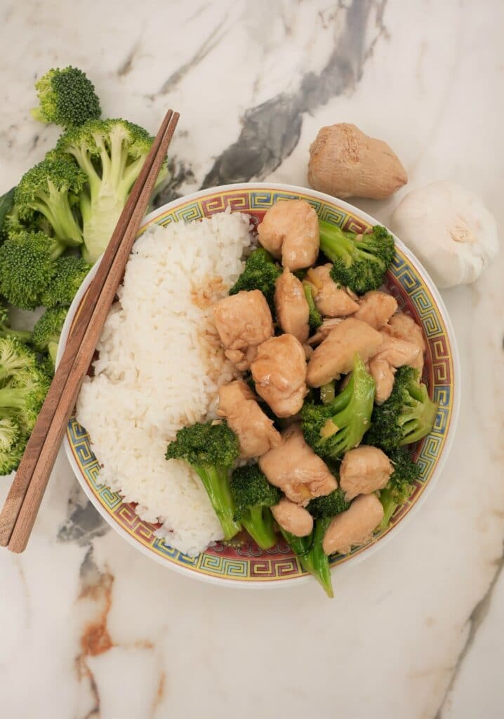 A plate of chinese chicken and broccoli next to a side of white rice.