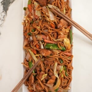 Chicken lo mein plated on a rectangular tray next to chopsticks.