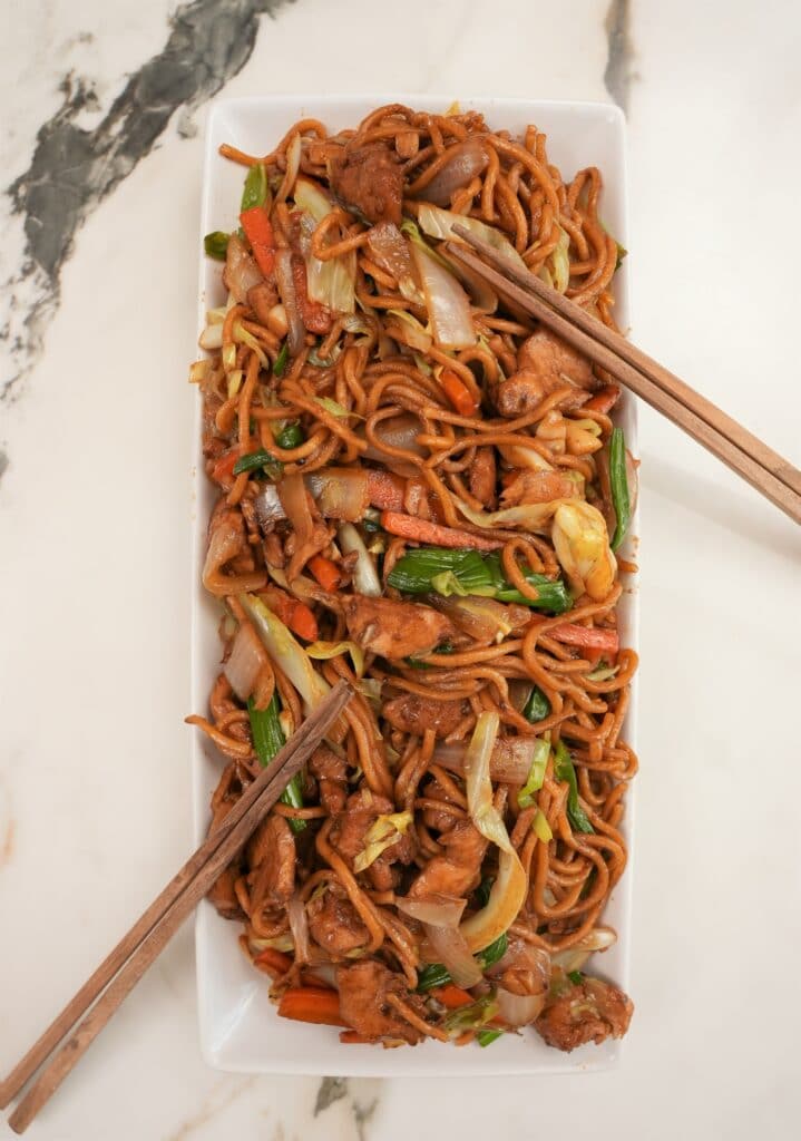 A photo of Chicken Lo Mein plated on a rectangular tray with chopsticks.
