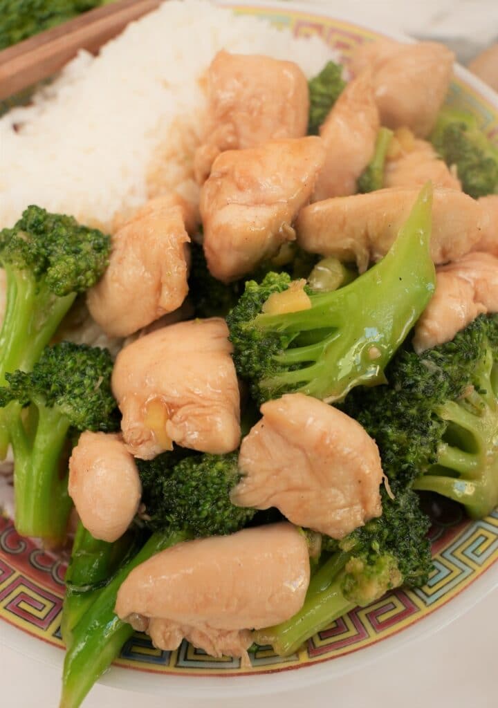 Chinese chicken and broccoli on a plate next to a side of white rice.