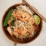Pad Thai plated in a wooden bowl with lime, bean sprouts, and green onion.