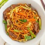 A bowl of beef lo mein with a pair of chopsticks.