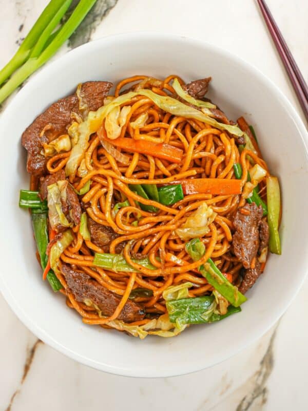 A bowl of beef lo mein with a pair of chopsticks.