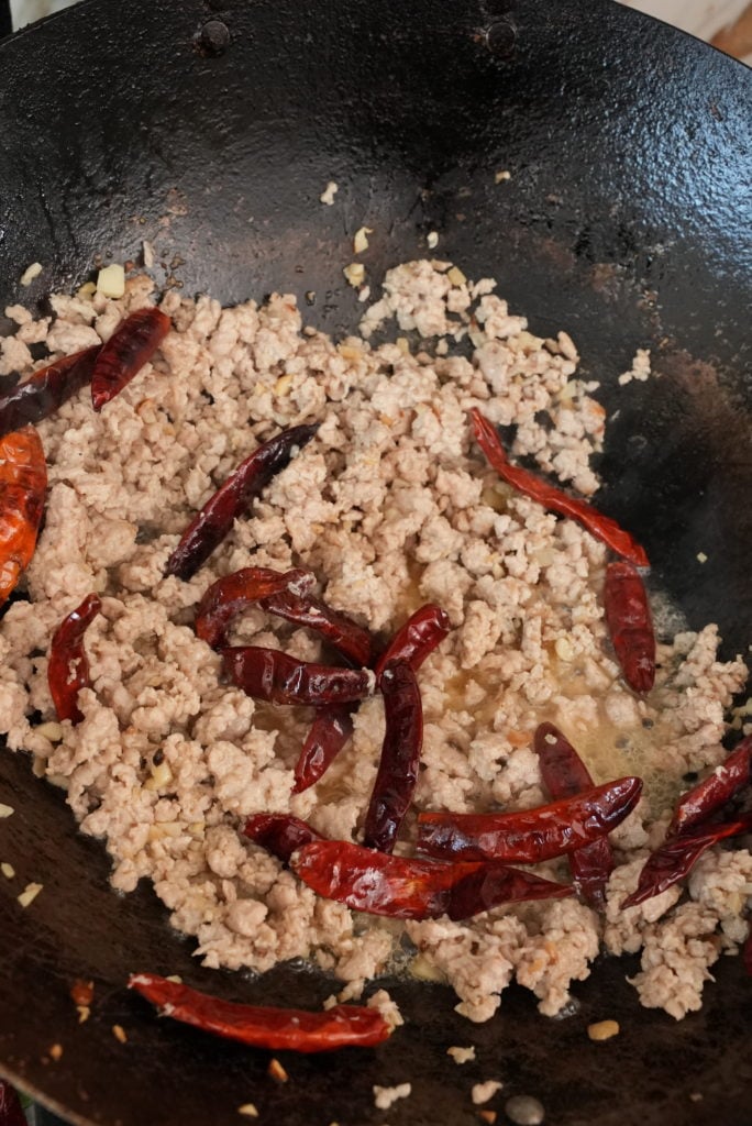 ground pork cooking in a pan with chilis and garlic