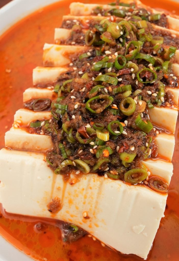 Chilis with scallions, soy sauce, and sesame oil topped over soft tofu on a plate.