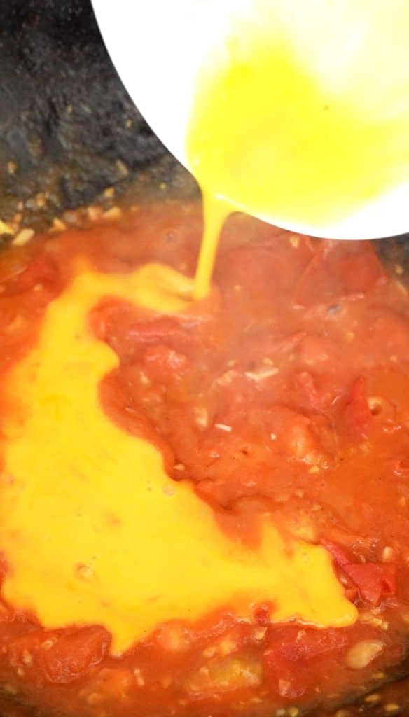 Beaten egg being poured into stir fried tomatoes.