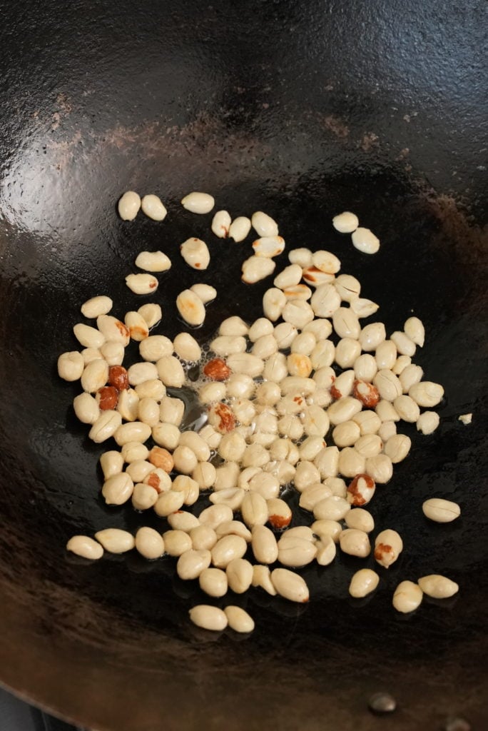 Peanuts frying in a wok with oil.