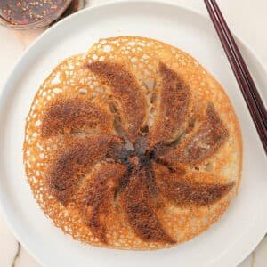 A perfect crispy dumpling skirt on a plate with chopsticks and dumpling dipping sauce.