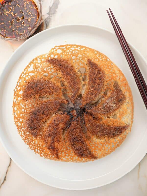 A perfect crispy dumpling skirt on a plate with chopsticks and dumpling dipping sauce.