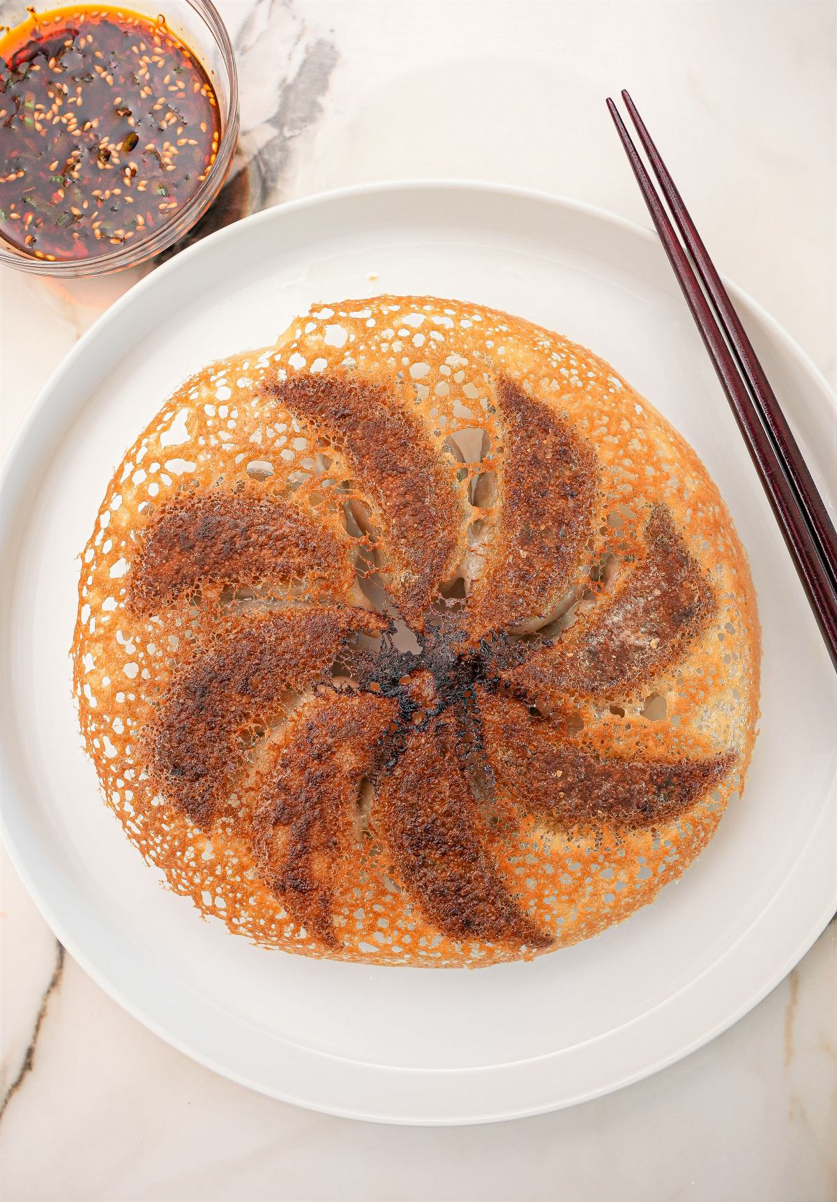 A perfect crispy dumpling skirt on a plate with chopsticks and dumpling dipping sauce.