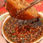 Dumpling dipping sauce with a dumpling being held by chopsticks.