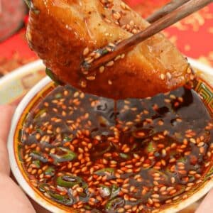 Dumpling dipping sauce with a dumpling being held by chopsticks.