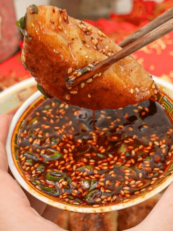 Dumpling dipping sauce with a dumpling being held by chopsticks.