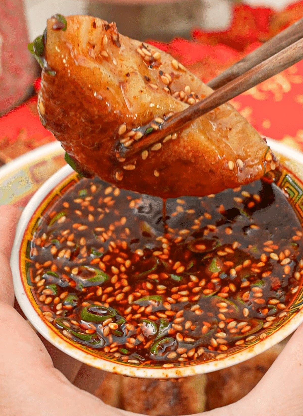Dumpling dipping sauce with a dumpling being held by chopsticks.