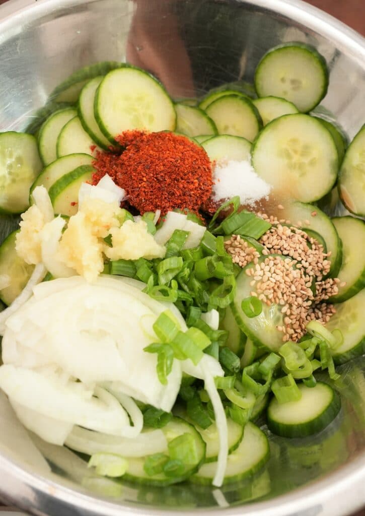 Thinly sliced cucumbers with korean cucumber salad ingredients in a bowl