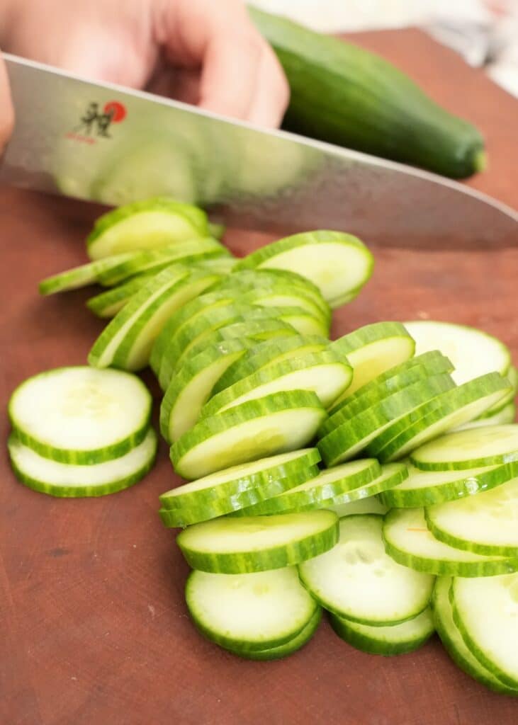 Thinly sliced cucumbers on a cutting board with a knife.