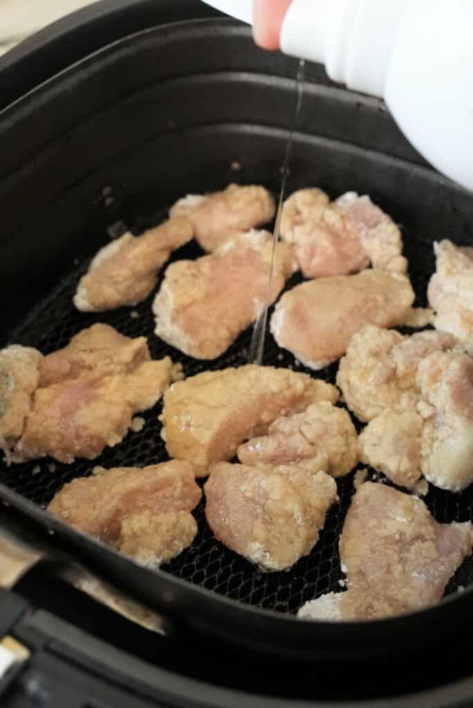 chicken thigh getting sprayed with oil in an air fryer