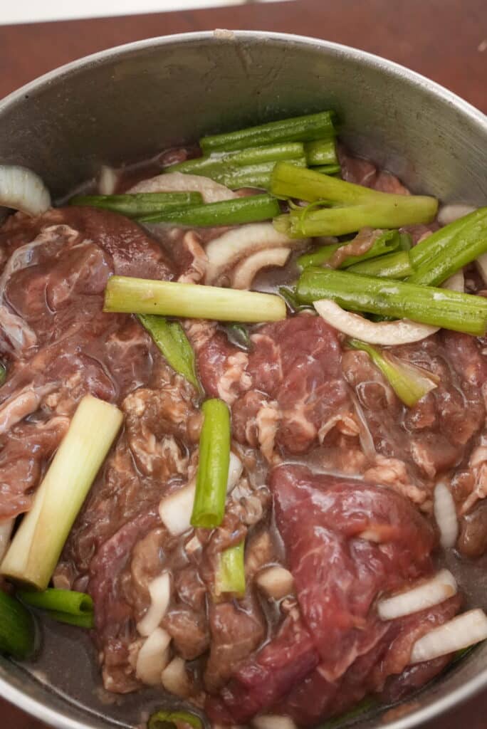 Thinly sliced beef marinating in a metal bowl