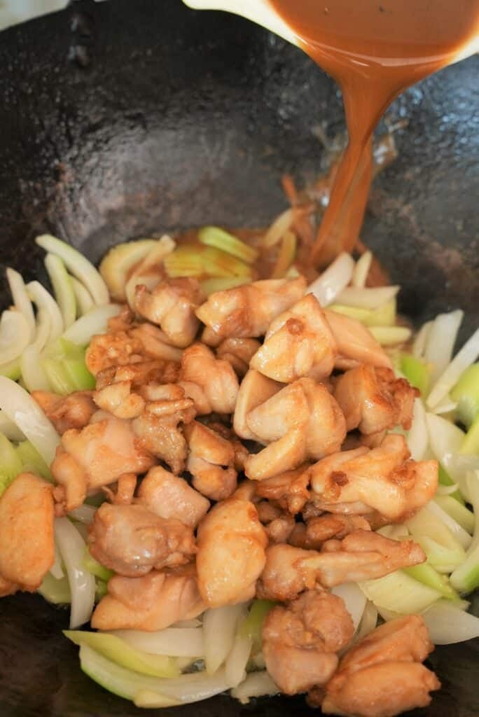 Black pepper chicken sauce being added to the wok with chicken and vegetables.