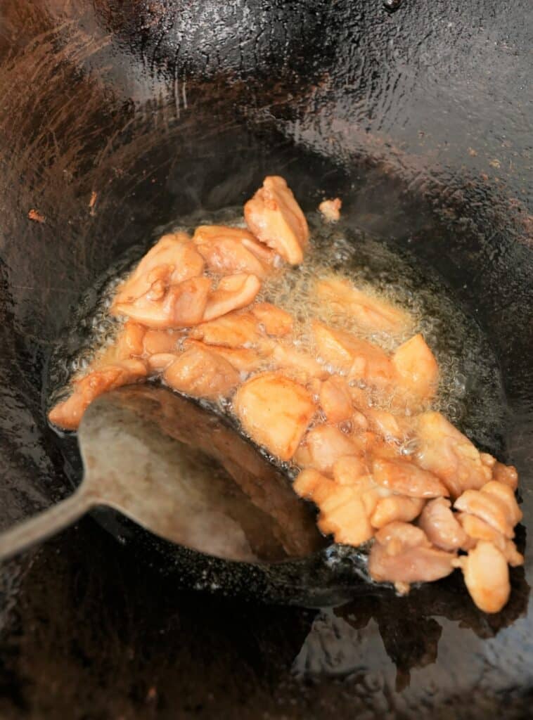 Frying marinated chicken pieces in a wok with oil.