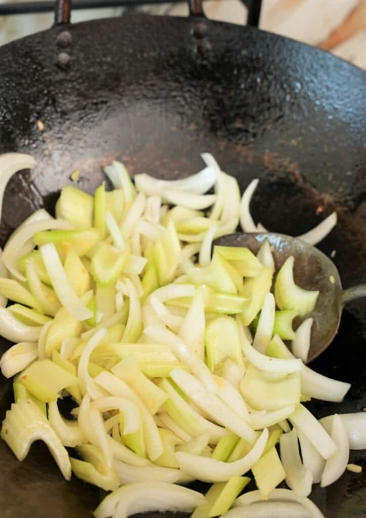 Celery and onions cooking in a wok with garlic and ginger.