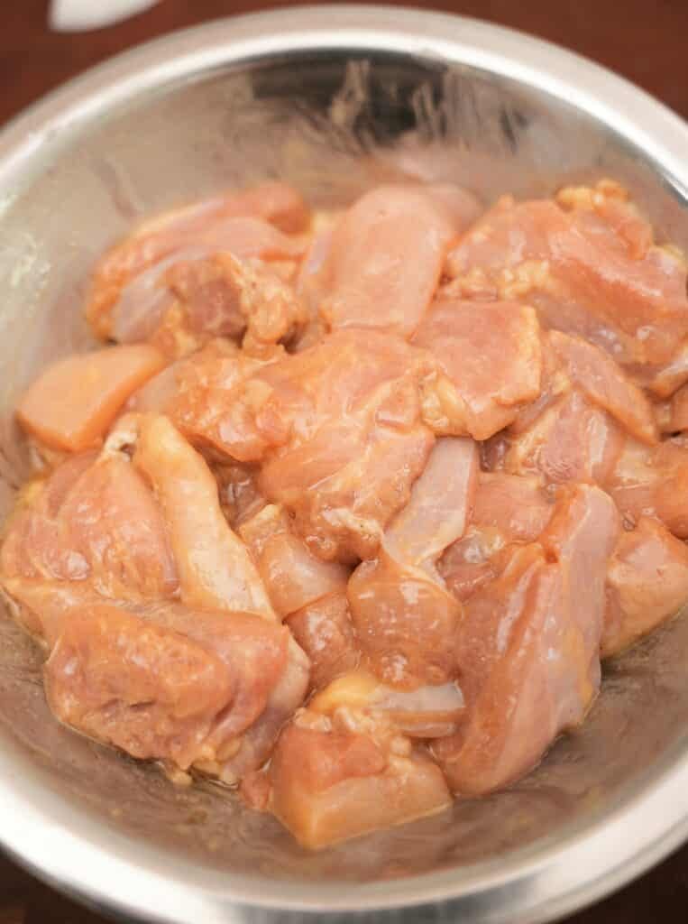 Chicken thigh marinating in a metal bowl.