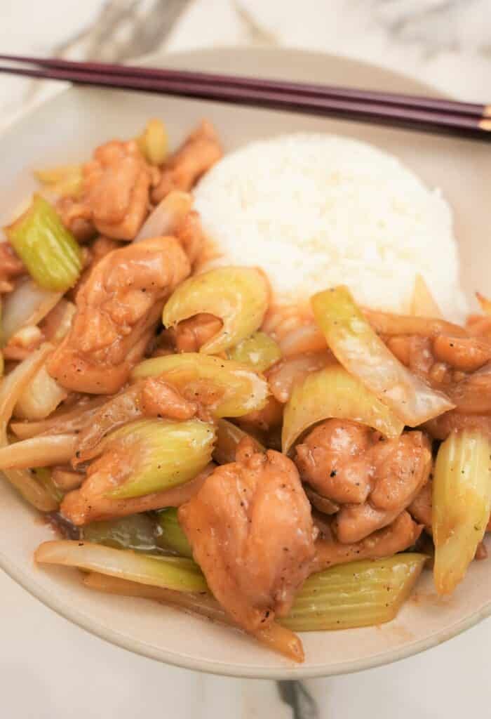 Black pepper chicken in a bowl with rice and chopsticks.