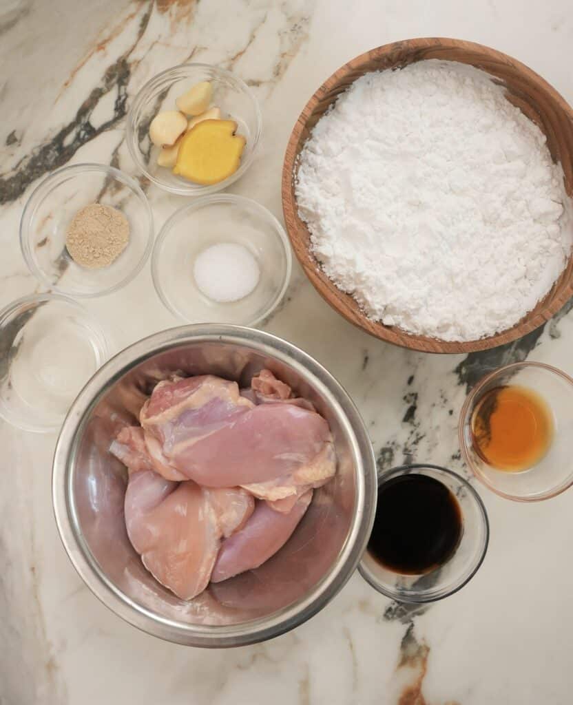 Raw ingredients for chicken karaage with garlic and ginger, sake, white pepper, salt, soy sauce, chicken thigh, sesame oil and potato starch.