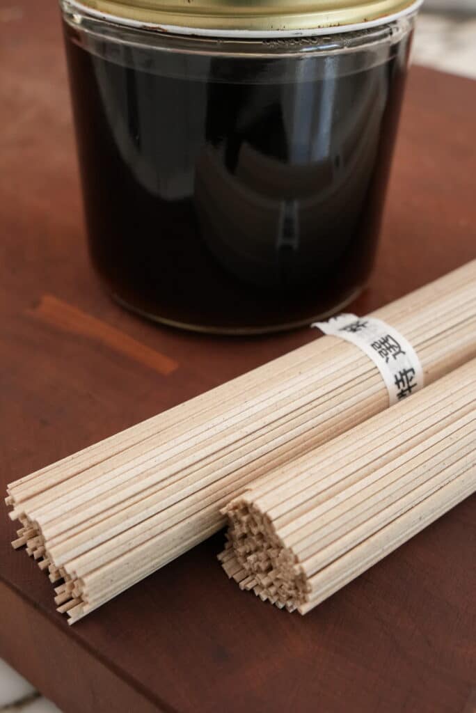 Dried soba noodles with sauce next to a jar of sauce.