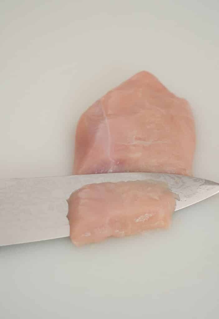 Thinly slicing chicken on a cutting board