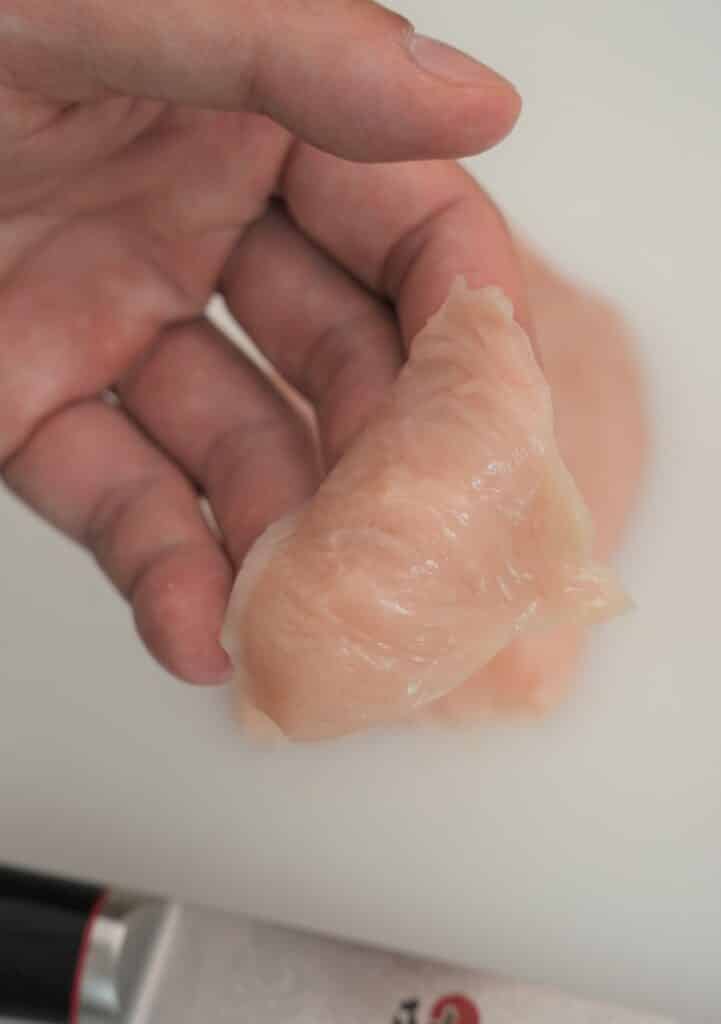 A piece of thinly sliced chicken holding in hand