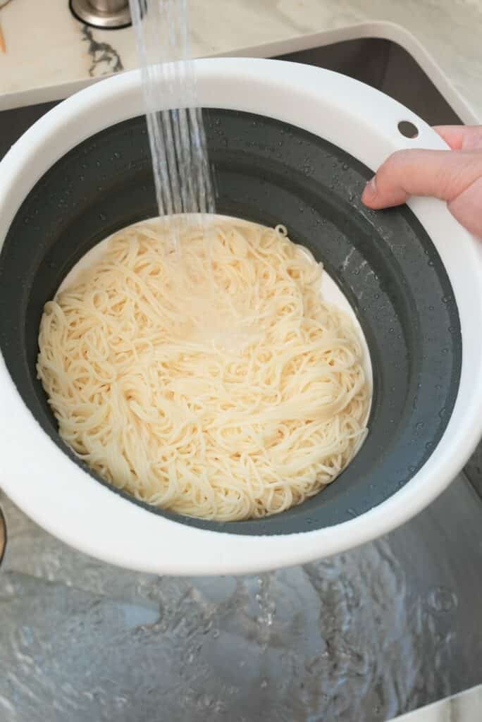 Rinsing noodles in a strainer under cold water.