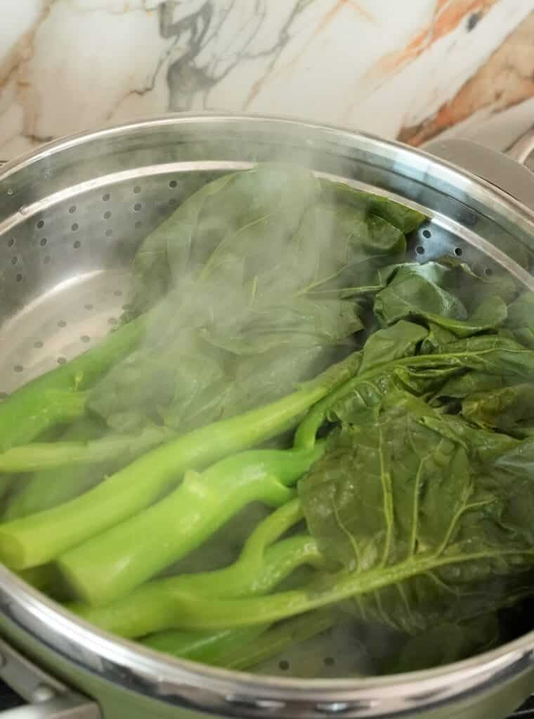 Gai lan steaming in a pan with the lid removed.