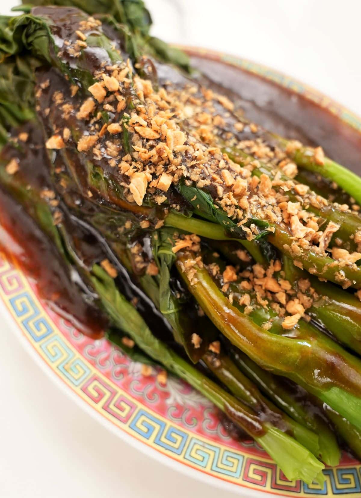 A plate of Gai Lan with Oyster Sauce topped with fried garlic on a plate.
