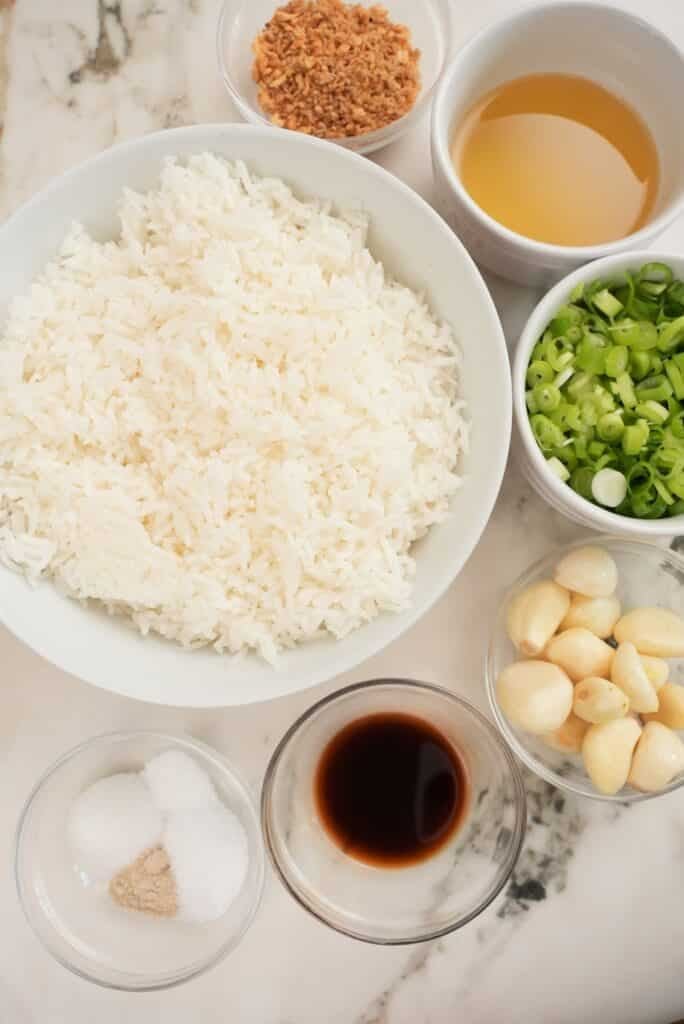 Ingredients for garlic fried rice in separate bowls on a table.