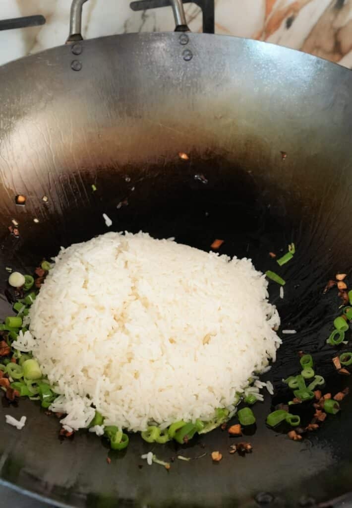 White rice added to garlic and scallions in a wok.