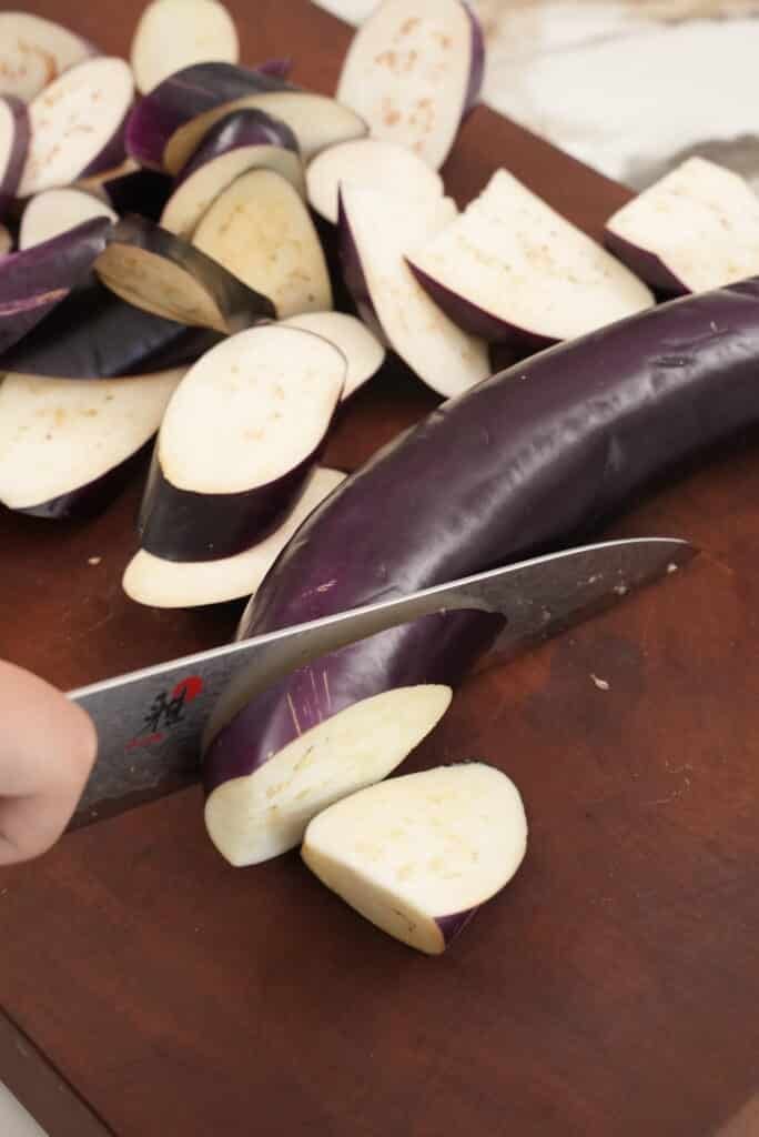 Cutting eggplant into pieces with a knife.