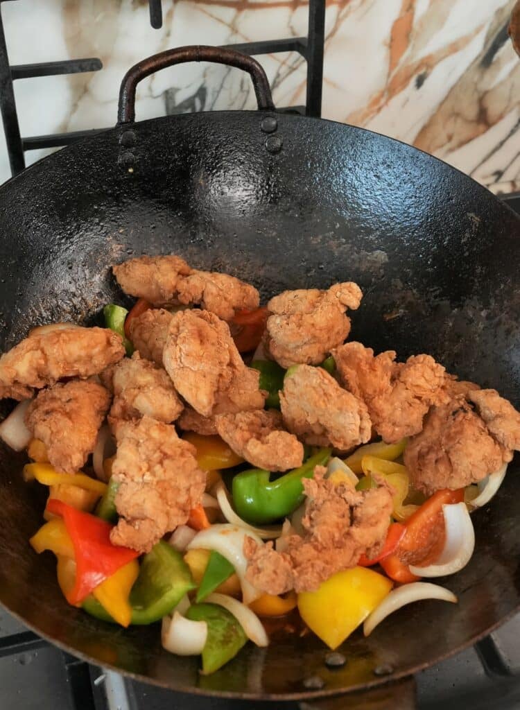 Adding chicken in the wok with peppers
