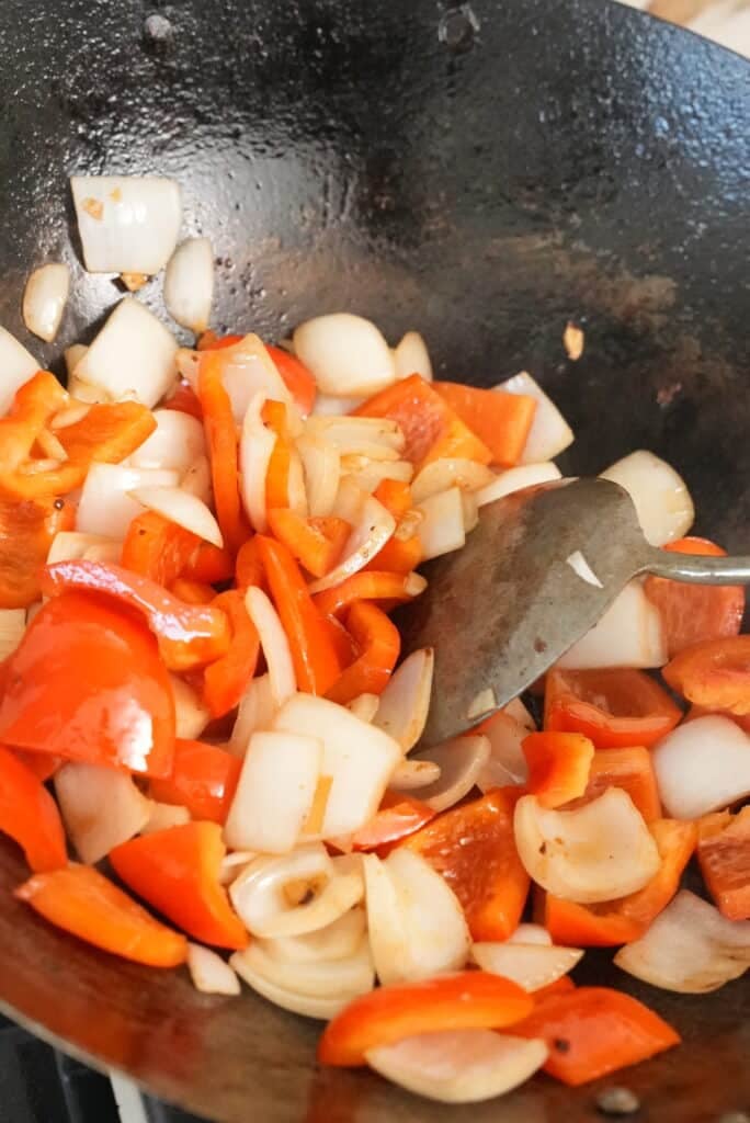 cooking onions, peppers, and garlic in a wok