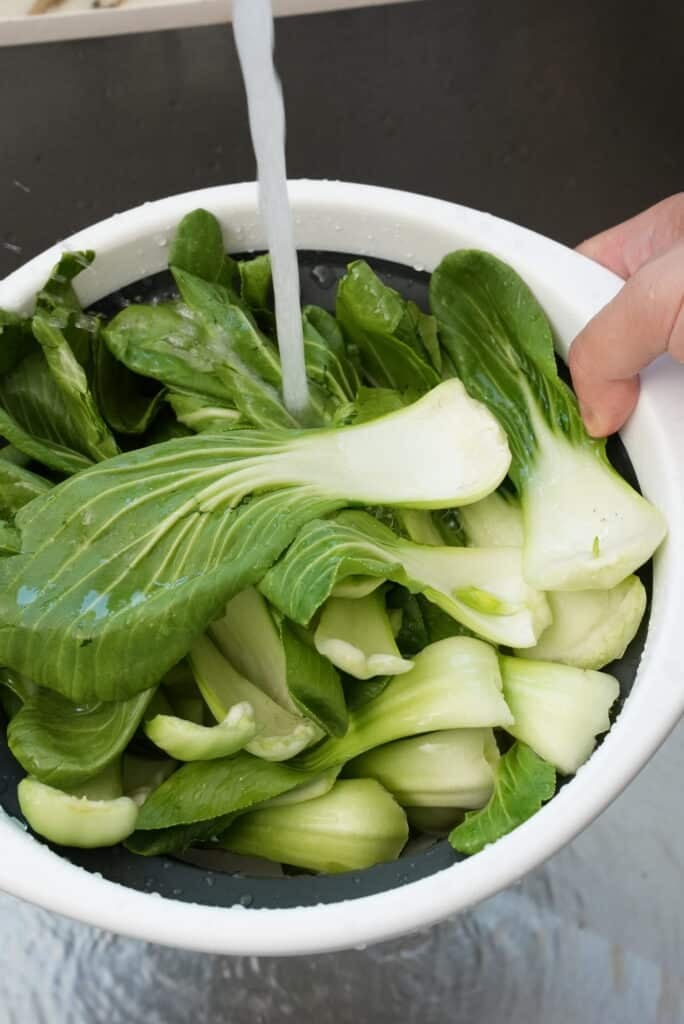 Rinsing bok choy with water in a strainer.