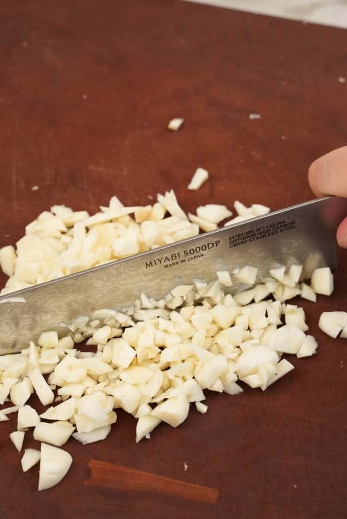 Mincing garlic on a cutting board.