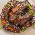 A pile of Sticky Asian Ribs in a bowl with scallions and sesame seeds