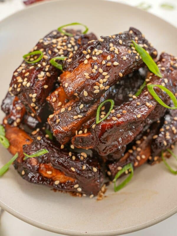 A pile of Sticky Asian Ribs in a bowl with scallions and sesame seeds