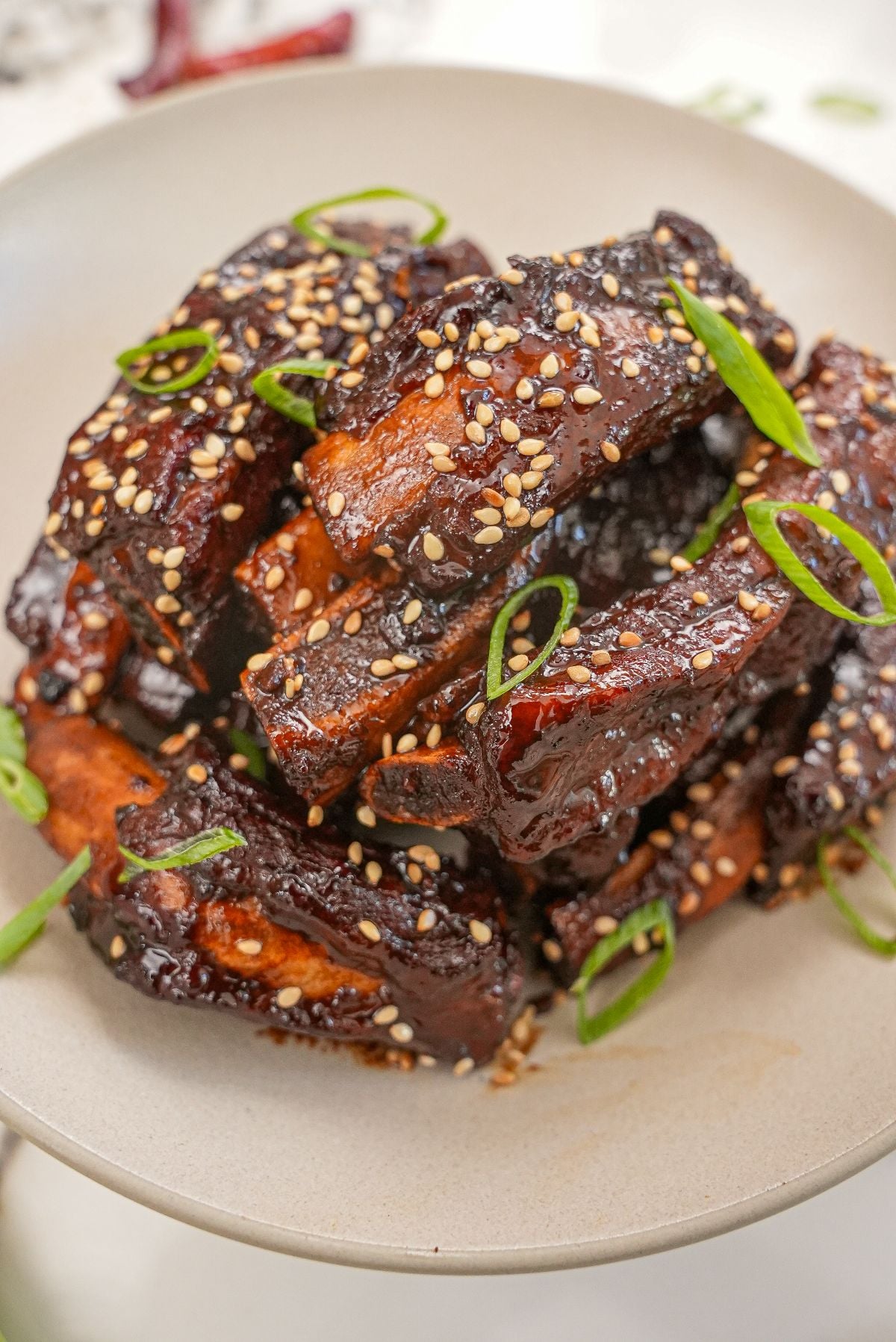 A pile of Sticky Asian Ribs in a bowl with scallions and sesame seeds