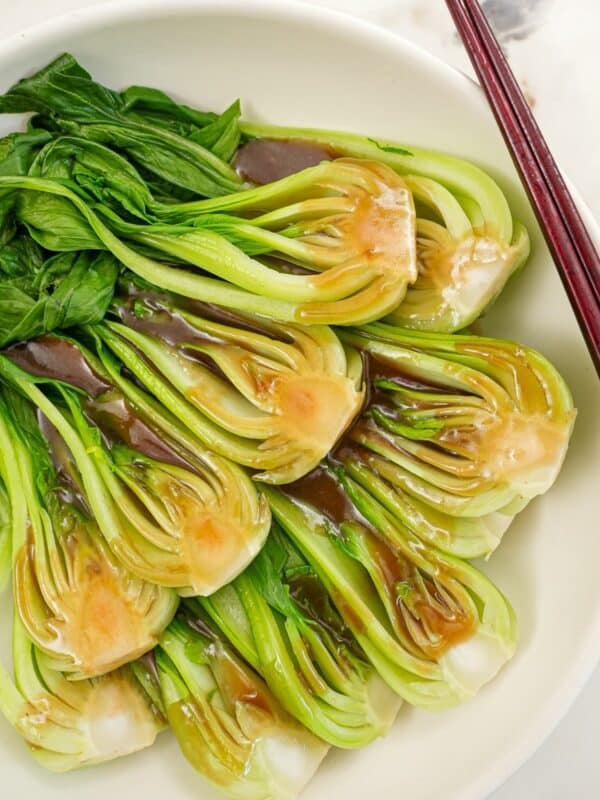 Bok Choy in a bowl with oyster sauce and a pair of chopsticks.