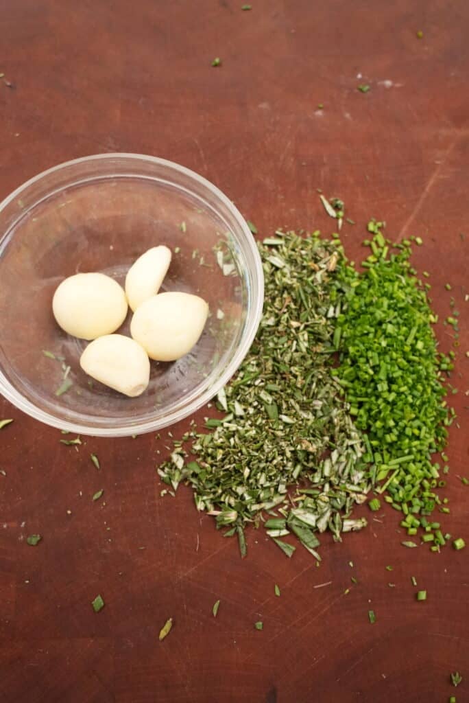 raw garlic with chopped herbs on a cutting board