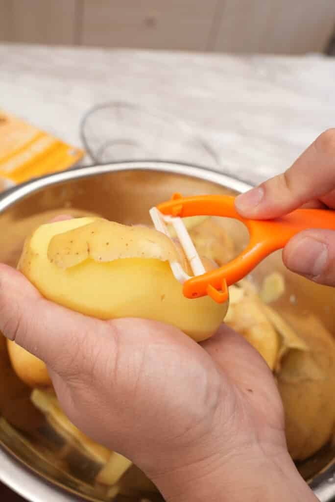 A potato peeler peeling the skin off of yellow potatoes.